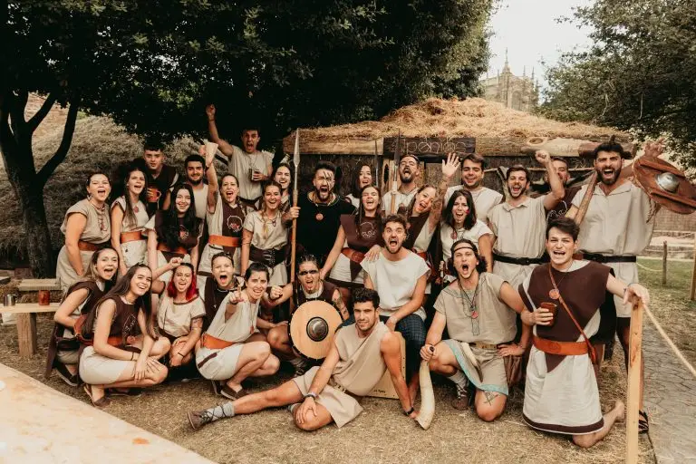 Foto grupal de la tribu astur Penios con túnicas beige y marrón, caetra y lanza, celebrando frente a su palloza en el poblado astur de Astorga